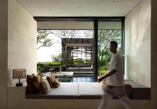 a man walking through a living room with a large couch at Alila Villas Uluwatu in Uluwatu