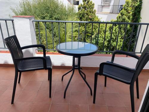 a glass table and two chairs on a balcony at NerjaRooms in Nerja