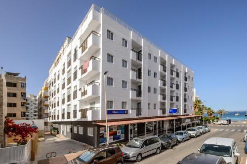 ein großes weißes Gebäude mit auf einem Parkplatz geparkten Autos in der Unterkunft Vibra Calima Apartamentos - Adults only in Sant Antoni de Portmany