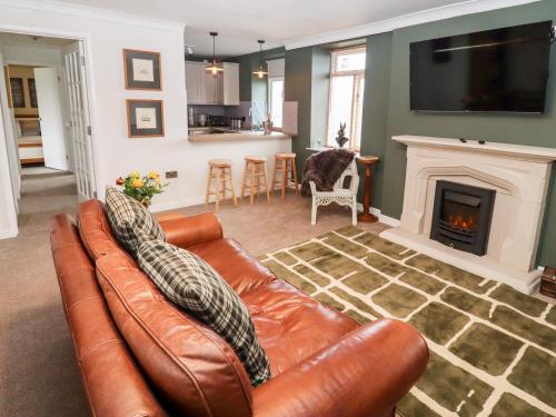a living room with a leather couch and a fireplace at The Carriage in Lydney