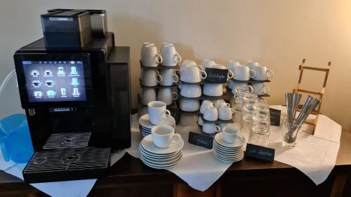 une table avec des tasses et des soucoupes à côté d'une machine à café dans l'établissement Hotel Cranach-Herberge City Centre, à Wittemberg