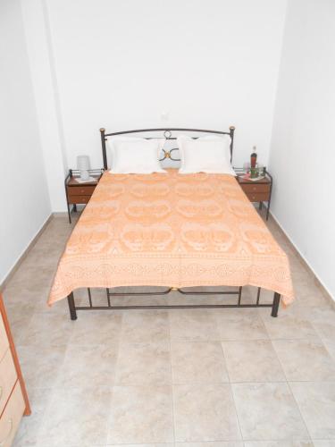 a bed with an orange comforter on top of it at Chrysolithos Kerami Apartments in Khalkíon