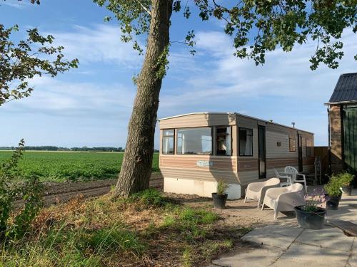 an rv parked next to a tree in a field at stacaravan Mientje in Hantum