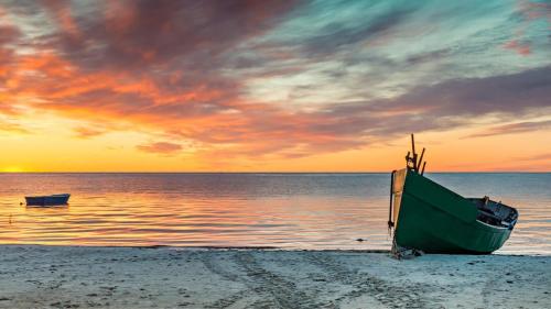 a green boat sitting on a beach with the ocean at Fewos Familie Krysik in Lühmannsdorf