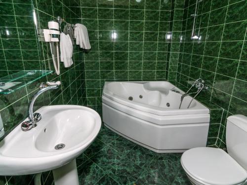 baño de azulejos verdes con bañera y lavamanos en Hotel VIP, en Tiflis