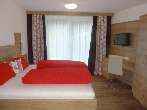 a bedroom with a large bed with red pillows and a television at Appartementhaus Naturquell in Sankt Leonhard im Pitztal