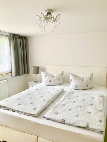 a white bedroom with two beds and a chandelier at Kuckuckswinkel- Ferienwohnung Lilian in Schöna