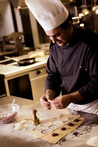 a man in a chef hat preparing food in a kitchen at Piz Galin Grand Hotel Family & Wellness in Andalo
