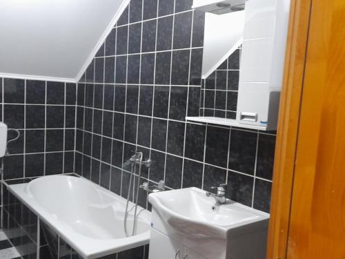 uma casa de banho em azulejos pretos com um lavatório e uma banheira em Pejovic em Višegrad
