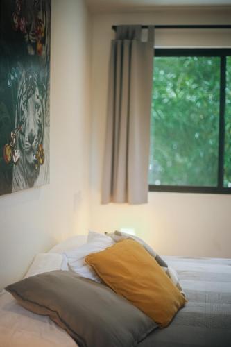 a bed with a yellow pillow and a window at El Hábita CASA SELVA in Santa Teresa Beach
