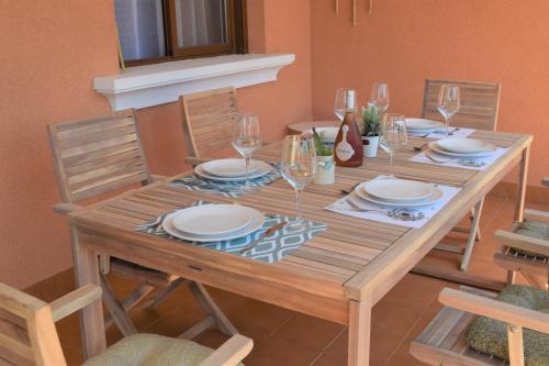 a wooden table with plates and wine glasses on it at Espacioso apartamento con preciosos jardines y BBQ in Isla Plana