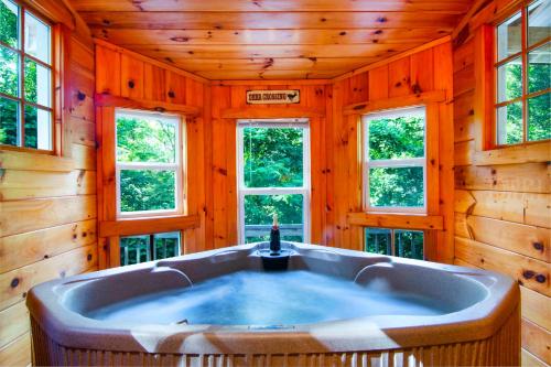 eine Badewanne in einem Zimmer mit Holzwänden und Fenstern in der Unterkunft Cozy Cabin Retreat - Hot Tub, Fireplace & Fire Pit in Blue Ridge