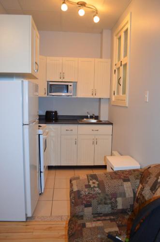 a kitchen with white cabinets and a couch in a room at Le Citadin in Rouyn
