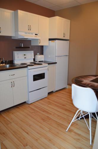 a kitchen with white appliances and a table and a chair at Le Citadin in Rouyn