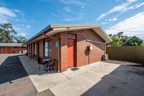 a brick building with a red door and chairs at Golden Country Motel and Caravan Park in Maryborough