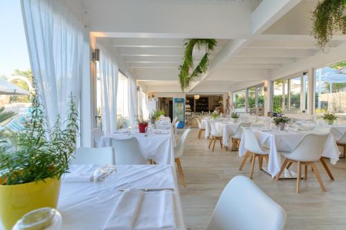 un restaurante con mesas y sillas blancas y ventanas en Malia Village en Vieste