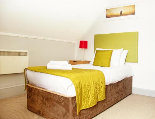 a bedroom with a large bed with a yellow blanket at The Portpatrick Hotel by Compass Hospitality in Portpatrick