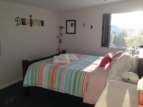 a bedroom with a bed with a striped blanket and a window at Stay in School by the Sea in Dunedin