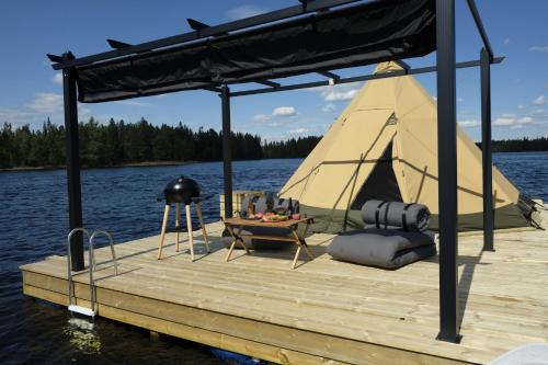 a dock with a tent and a table on the water at Tentipi River Camp in Sorsele