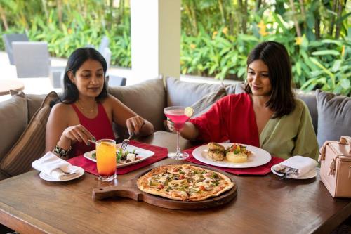 two women sitting at a table with a pizza at Alila Diwa Goa - A Hyatt Brand in Majorda