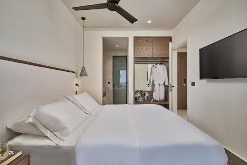 a white bedroom with a large bed and a flat screen tv at Ios Grand Pool Suites in Mylopotas