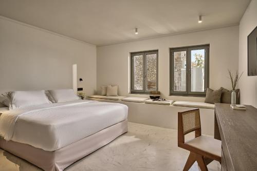 a white bedroom with a large bed and a desk at Ios Grand Pool Suites in Mylopotas