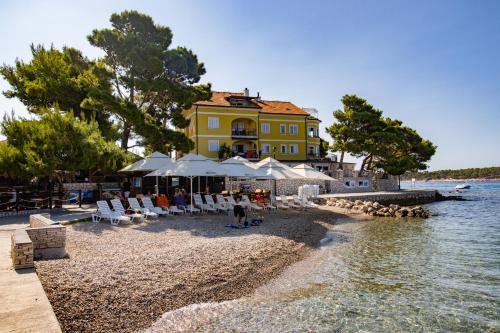 un edificio giallo su una spiaggia con sedie e acqua di Villa Petrac - App5 & App5A a Rab