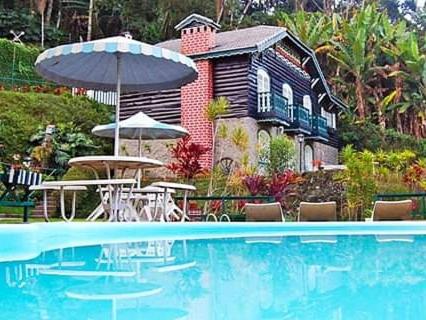 a swimming pool with an umbrella and a house at Nova Pousada Chamonix in Teresópolis