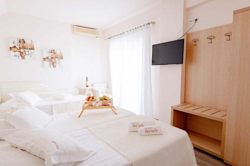 a white bedroom with two beds and a flat screen tv at Vournelis Beach Hotel and Spa in Iraklitsa