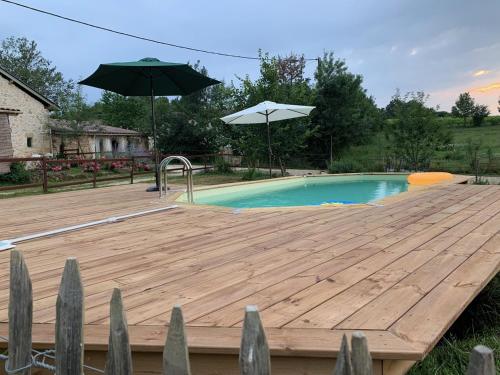 une terrasse en bois à côté d'une piscine avec un parasol dans l'établissement La Grange d'Oustaud, à Vérac