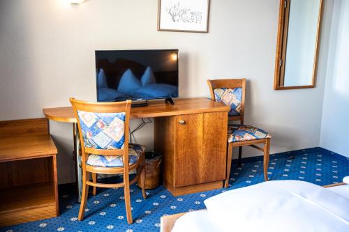 a room with a desk with a television and two chairs at PanoramaHotel Penegal in Mendola