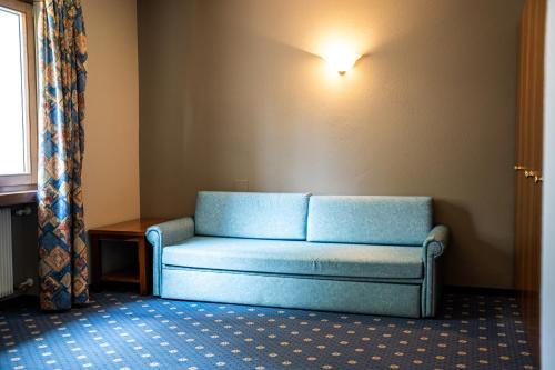 a blue couch sitting in a room with a window at PanoramaHotel Penegal in Mendola