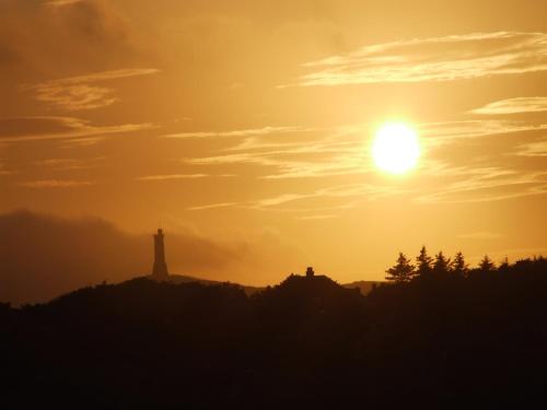 a sunset with a lighthouse on a hill at Ramadale Stornoway in Stornoway