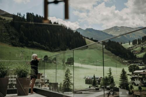 uma mulher de pé numa varanda com vista para uma montanha em Hotel VIEW - incl Joker Card in Summer em Saalbach Hinterglemm