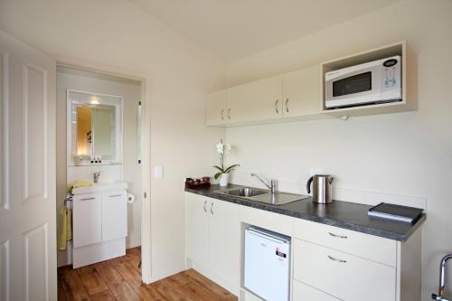 a white kitchen with a sink and a microwave at Auckland Country Cottages in Clevedon