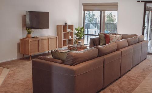 a living room with a brown couch and a flat screen tv at 50 HALE HAVEN in Stanthorpe