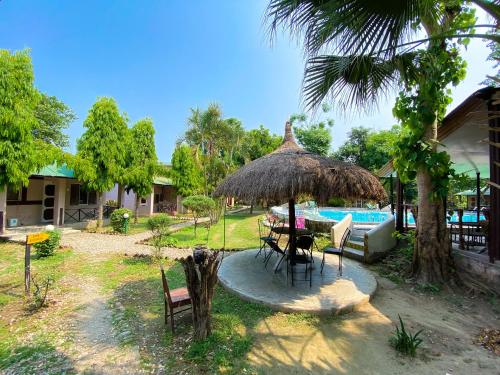 patio ze stołem i słomianym parasolem w obiekcie Nature Safari Camp w mieście Chitwan