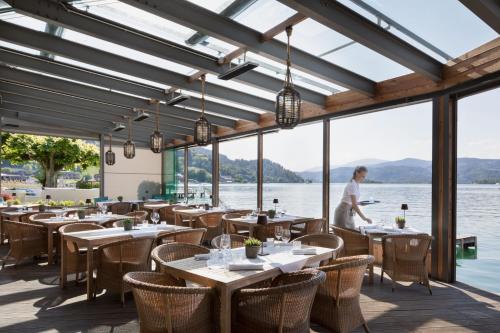 a restaurant with tables and chairs with a view of the water at Hotel Linde in Maria Wörth