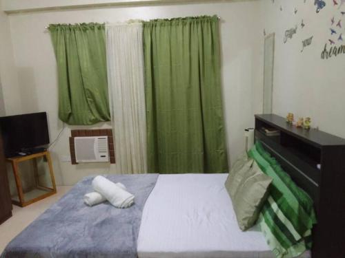 a bedroom with a bed with green curtains and a television at Studio for Rent near Ortigas Extension in Cainta