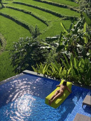 a woman laying on a raft in a swimming pool at Villa di Bias in Tirtagangga