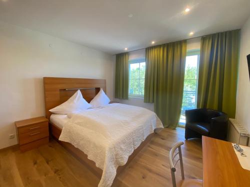 a bedroom with a bed and a chair and windows at Seehotel Herlinde in Podersdorf am See