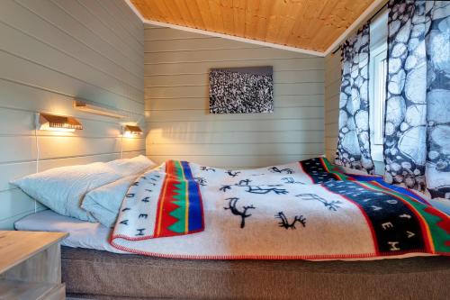 1 dormitorio con cama con edredón y ventana en Davvi Siida - Reindeer Design Lodge, en Kjøllefjord