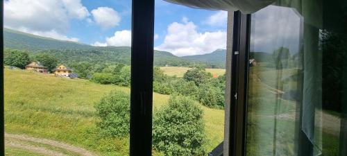 a window with a view of a field and mountains at ŁOMIANKOWA DOLINA Wetlina 112 in Wetlina