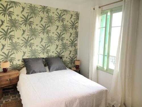 - une chambre avec un lit blanc et un papier peint tropical dans l'établissement Maison de charme en bord de Mer, au Barcarès