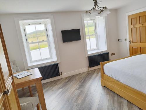 a bedroom with a bed and two windows and a desk at Biddy Ban’s in Carnmalin