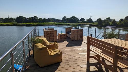 une terrasse en bois avec des chaises et un banc sur l'eau dans l'établissement Hausboot Wangermeerblick (Floating Home), à Wangerland