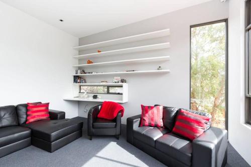 a living room with black leather couches and red pillows at Luxurious, Tranquil and Private in Lindisfarne