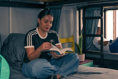 a woman sitting on a bed reading a book at Chillout Hostel Barrio Escalante in San José