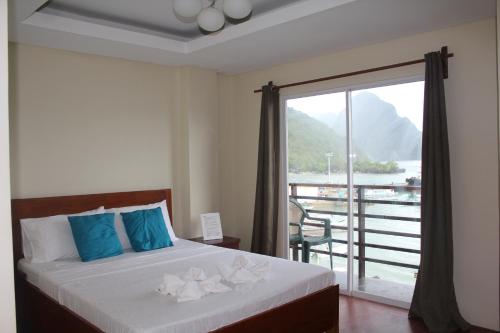 a bedroom with a bed with blue pillows and a balcony at Aqua Travel Lodge in El Nido