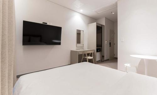 a white bedroom with a bed and a tv on the wall at H Avenue Hotel Idae Shinchon in Seoul